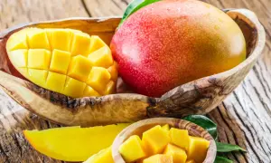 Dwa soczyste mango, jedno w całości, drugie pokrojone w kostkę, w drewnianych miseczkach. Idealne na zdrową przekąskę, mango kcal to ok. 60 na 100g.