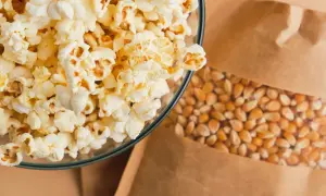 Miseczka puszystego popcornu obok ziaren kukurydzy w papierowej torbie. Zastanawiasz się nad popcorn kcal?