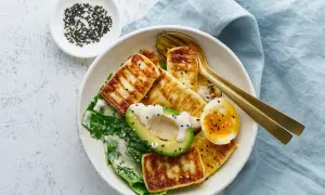 Sałatka z grillowanym serem halloumi, awokado, jajkiem i zielonymi liśćmi, posypana sezamem.