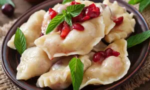 Pyszne, domowe ciasto na pierogi pieczone w piekarniku, podane z wiśniami i miętą.