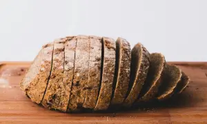 Pokrojony bochenek ciemnego chleba na desce. Każda kromka chleba kcal jest widoczna, posypana mąką.