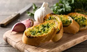 Chrupiąca bagietka czosnkowa z ziołami, obok czosnek i natka. Pyszna przekąska, warto sprawdzić jej bagietka czosnkowa kcal.