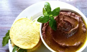 Miseczka pasty z fasoli adzuki z oliwą i listkami bazylii obok placków z rukolą.