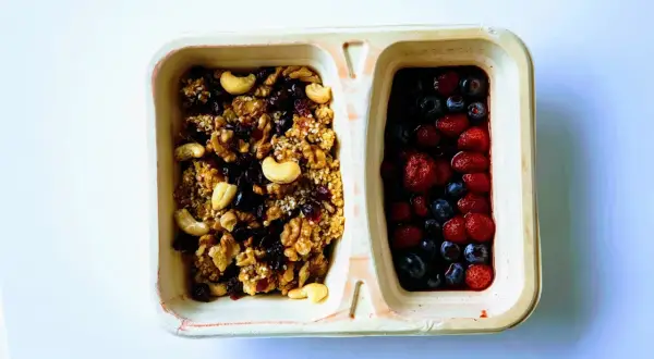 Dwie przegródki pojemnika: jedna z granolą z orzechami i suszonymi owocami, druga z jagodami i truskawkami. Czy kasza jaglana ma gluten? Ta granola jest bezglutenowa!