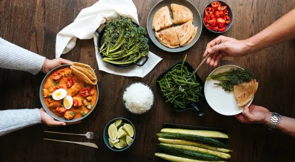 Stół z daniami: curry z kurczakiem, ryżem, brokułami, fasolką szparagową, ogórkami, limonkami i plackami.