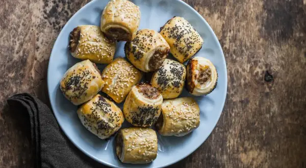 Paszteciki z ciasta francuskiego posypane sezamem i makiem na niebieskim talerzu.