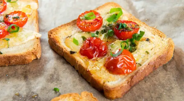 Pyszna, zdrowa kolacja: grzanki z roztopionym serem, pieczonymi pomidorkami koktajlowymi i szczypiorkiem.