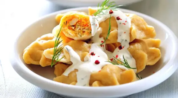 Pierogi z farszem warzywnym polane sosem, udekorowane koperkiem i pieprzem.