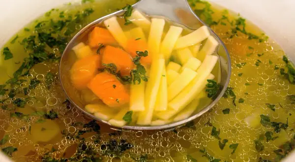 Łyżka nabiera porcję pysznego, aromatycznego rosołu wegetariańskiego z marchewką i makaronem.
