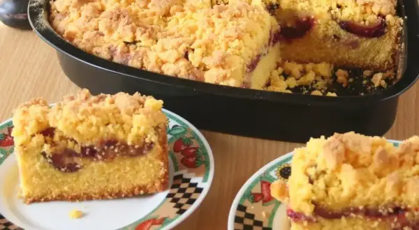 Pyszne ciasto z mąki kukurydzianej z soczystymi śliwkami i kruszonką. Dwa kawałki na talerzykach, reszta w formie.