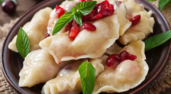 Pyszne, domowe ciasto na pierogi pieczone w piekarniku, podane z wiśniami i miętą.