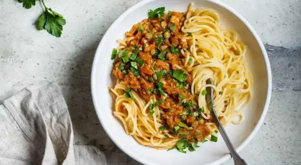 Porcja spaghetti z sosem z soczewicy i warzyw, posypana natką pietruszki. Pyszne i zdrowe spaghetti kcal.