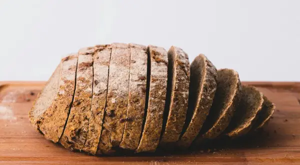 Pokrojony bochenek ciemnego chleba na desce. Każda kromka chleba kcal jest widoczna, posypana mąką.