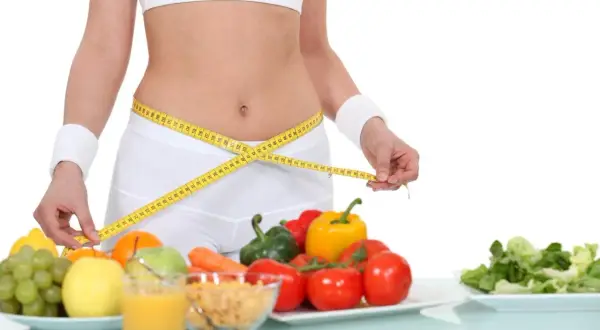 Kobieta mierzy talię centymetrem. Obok zdrowe jedzenie: owoce, warzywa, płatki. Dieta 1500 kcal efekty w zasięgu ręki!
