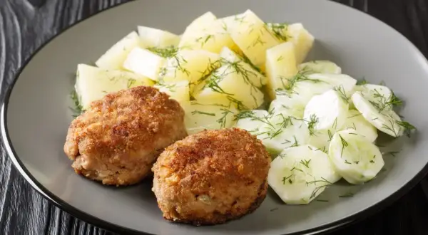Dwa kotlety mielone z ziemniakami i mizerią na talerzu.