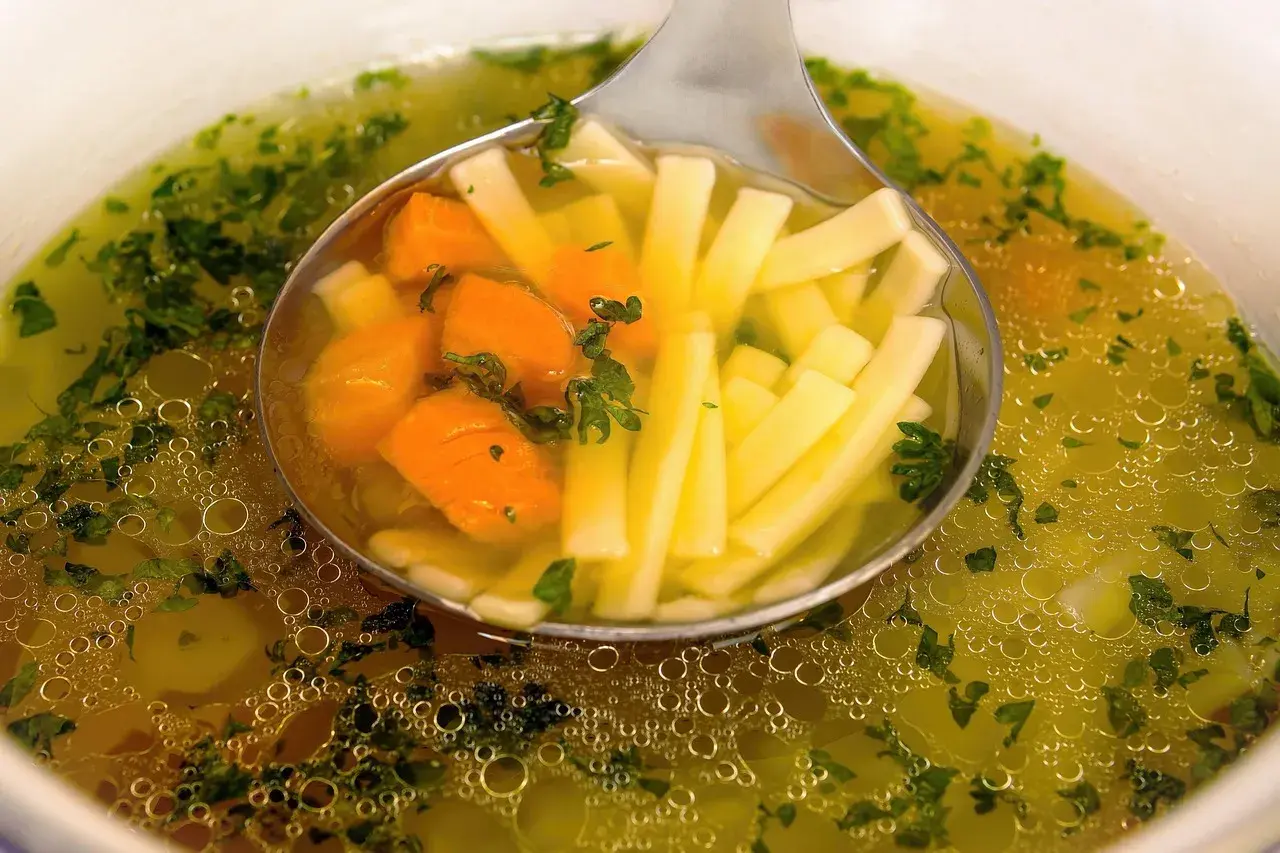 Łyżka nabiera porcję pysznego, aromatycznego rosołu wegetariańskiego z marchewką i makaronem.