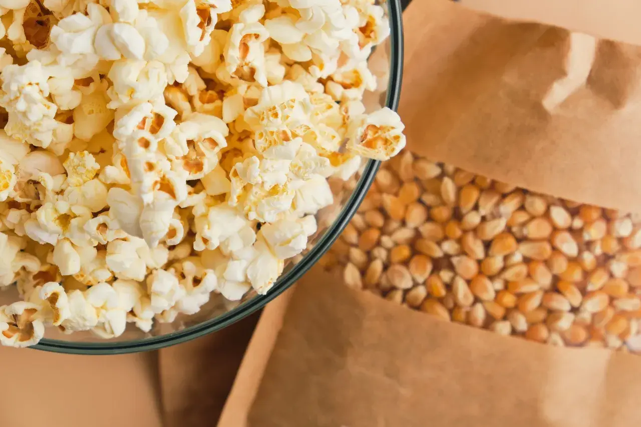 Miseczka puszystego popcornu obok ziaren kukurydzy w papierowej torbie. Zastanawiasz się nad popcorn kcal?