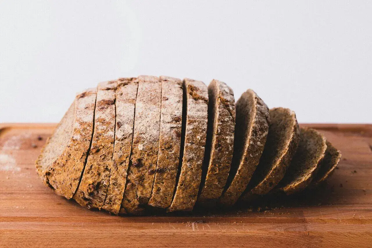 Pokrojony bochenek ciemnego chleba na desce. Każda kromka chleba kcal jest widoczna, posypana mąką.