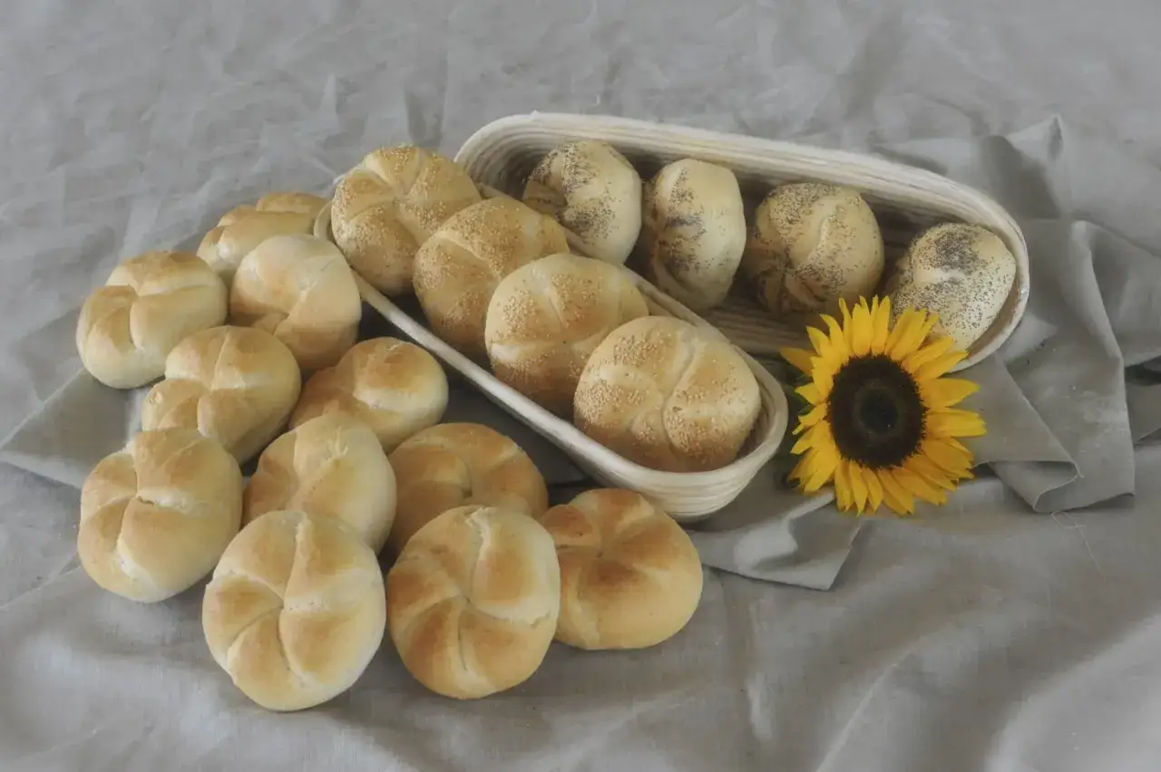 Świeże kajzerki, niektóre posypane sezamem, inne makiem, leżą obok słonecznika. Ile kcal ma taka kajzerka?
