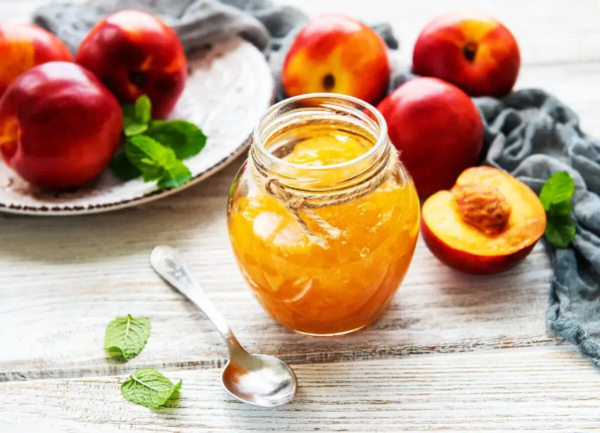 Słoik domowego dżemu z nektarynek, obok świeże owoce i listki mięty. Idealny na zdrowe śniadanie, z niską zawartością nektarynka kcal.