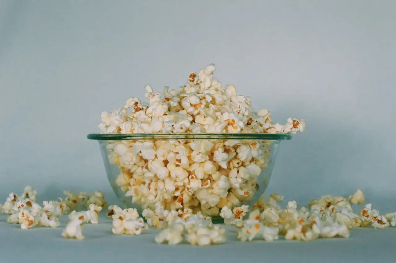 Góra popcornu w szklanej misce, rozsypane ziarna wokół. Idealna przekąska, ale warto pamiętać o popcorn kcal.