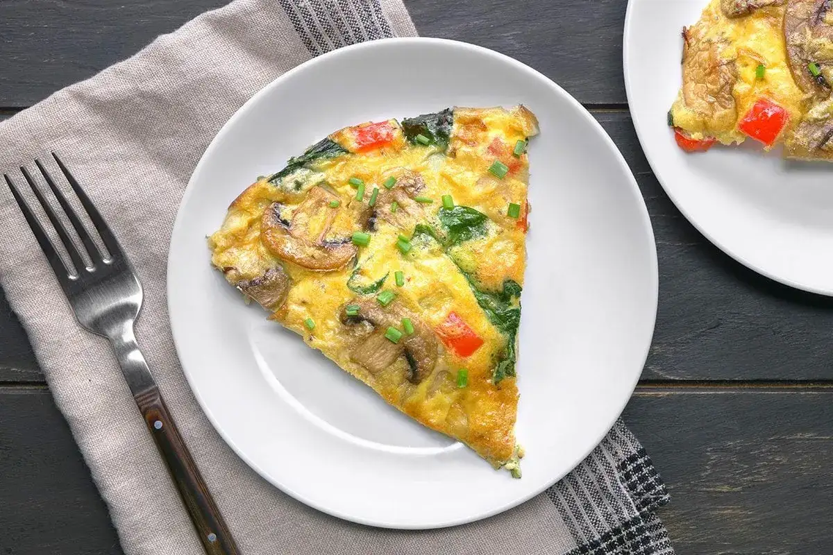 Pyszny omlet z pieczarkami, szpinakiem i papryką. Idealne śniadanie bez węglowodanów, podane na białym talerzu z widelcem obok.