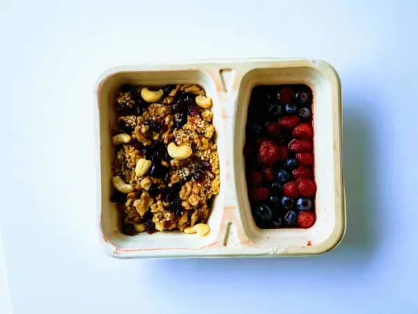 Dwie przegródki pojemnika: jedna z granolą z orzechami i suszonymi owocami, druga z jagodami i truskawkami. Czy kasza jaglana ma gluten? Ta granola jest bezglutenowa!