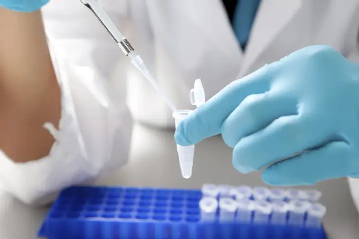 Ręka w niebieskiej rękawiczce laboratoryjnej używa pipety do pobrania płynu z probówki.